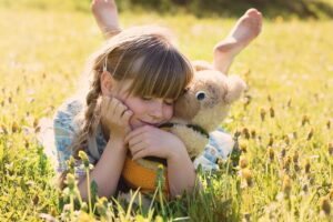 little girl snuggling with a teddy bear in a field